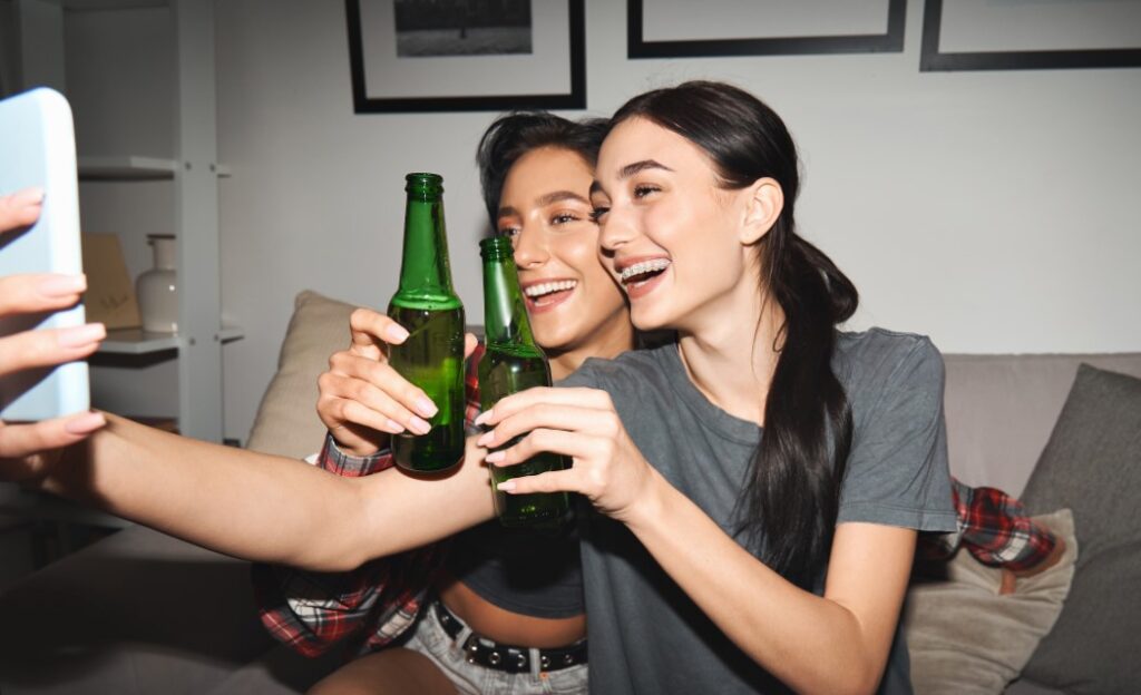 two-happy-young-girls-holding-phone-drinking-beer-online-activities